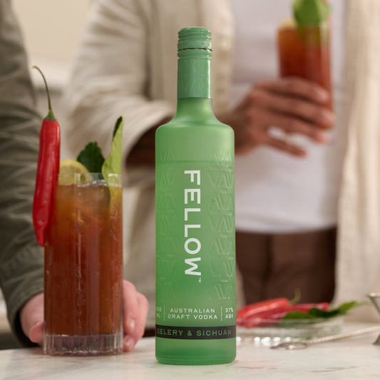 Green bottle of 'Fellow' celery & sichuan vodka with Bloody Mary cocktails on a table.