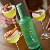 Green bottle labeled 'Fellow' with cocktails on a wooden table
