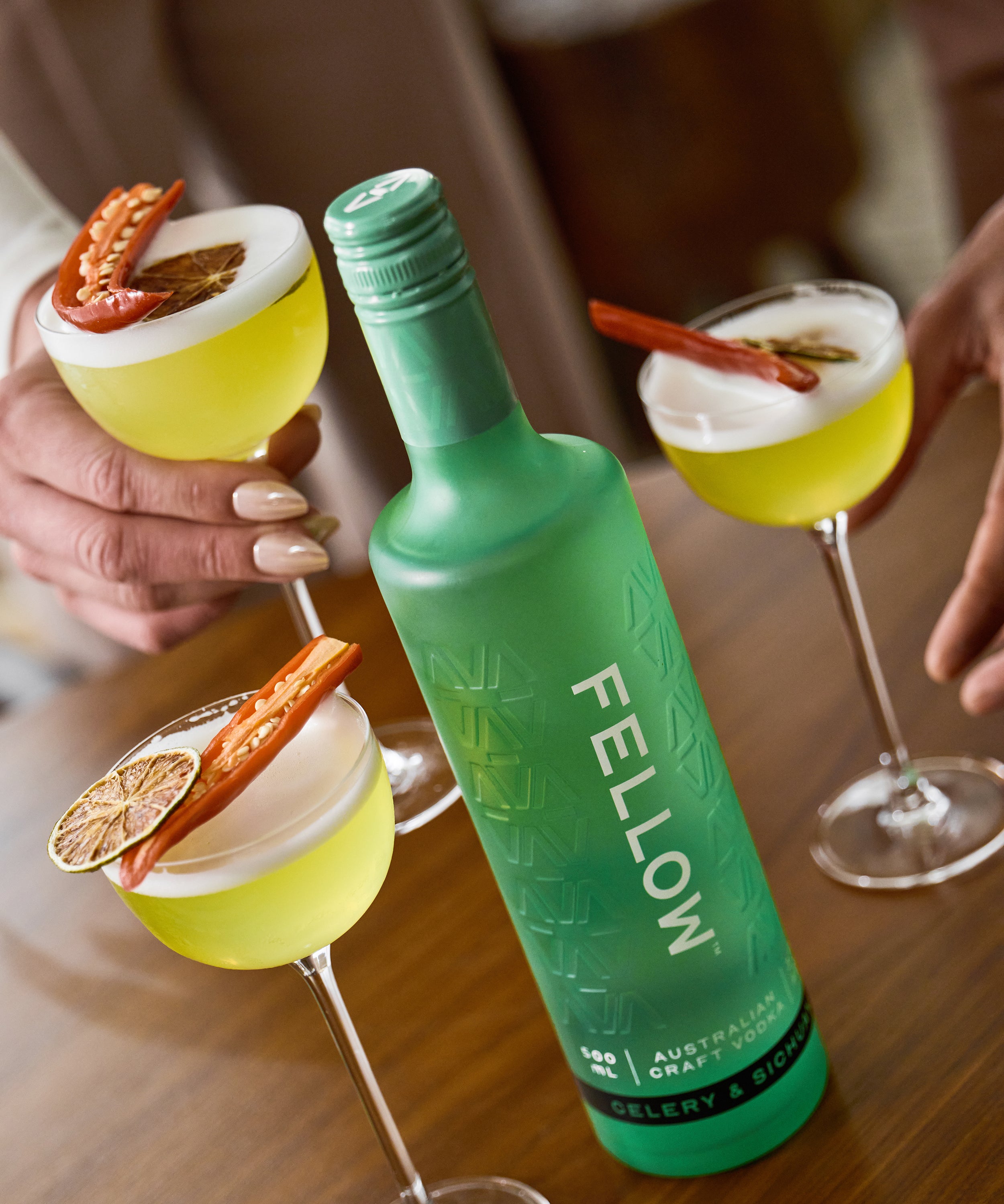 Green bottle labeled 'Fellow' with cocktails on a wooden table